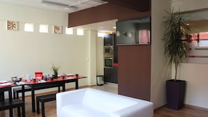 A modern living room with a white sofa, a dining table with red placemats, and a kitchen area in the background. - Bilbao Central Hostel (Bilbao)