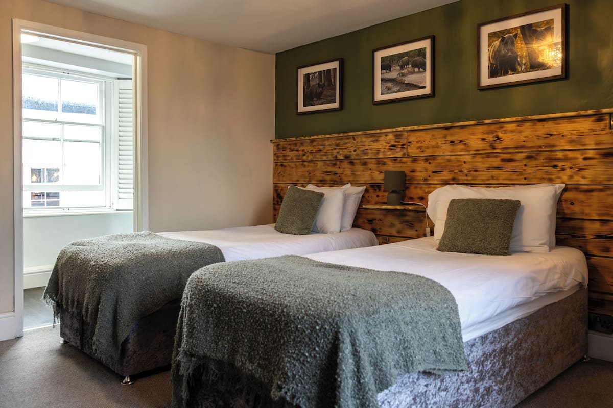 A room with two beds, a wooden headboard, and framed pictures on the wall.