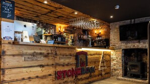 A rustic bar area with wooden walls, a stone fireplace, and a television mounted on the wall. - The First Hurdle Guest House (Chepstow)
