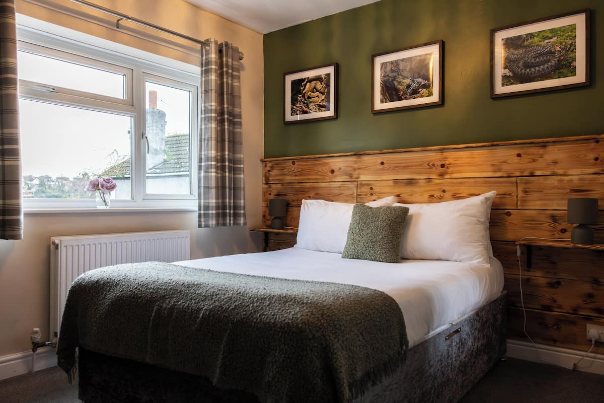 A neatly made bed with a green blanket, a wooden headboard, and two framed pictures on the wall.