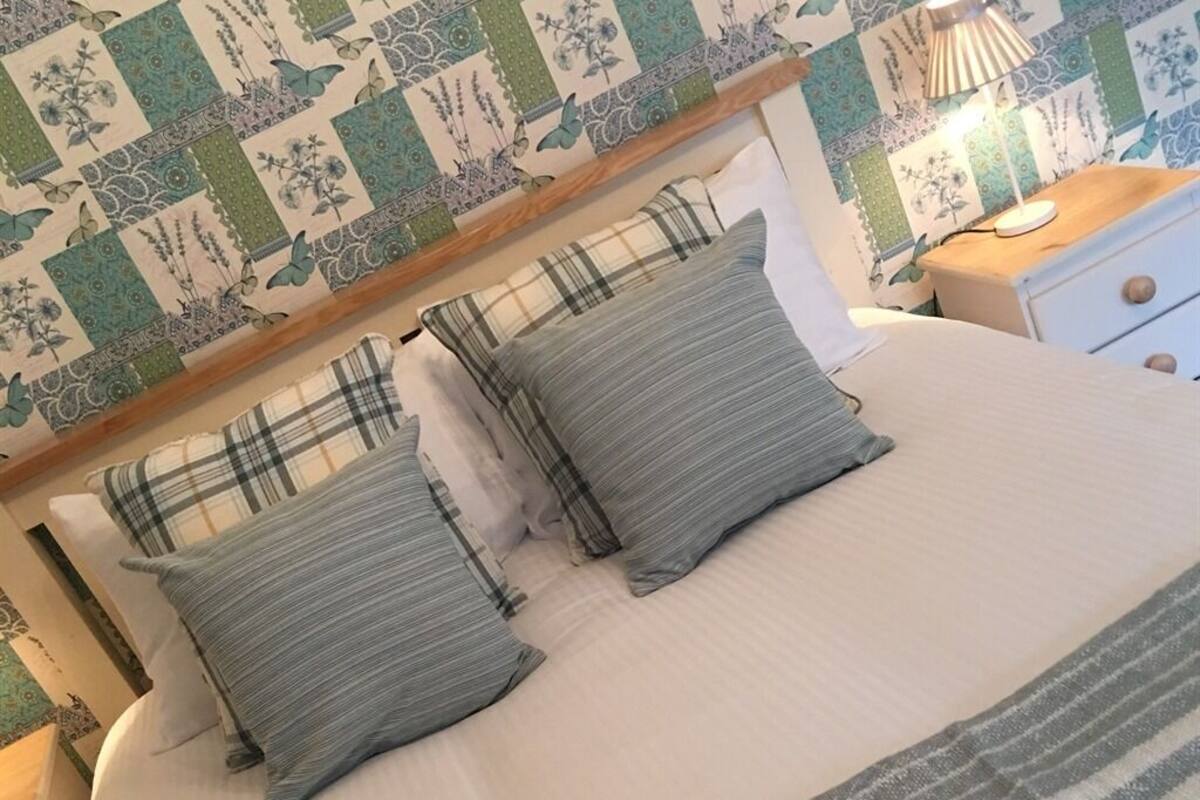 A bed with two pillows, a bedside table with a lamp, and a wall with a floral patterned wallpaper.