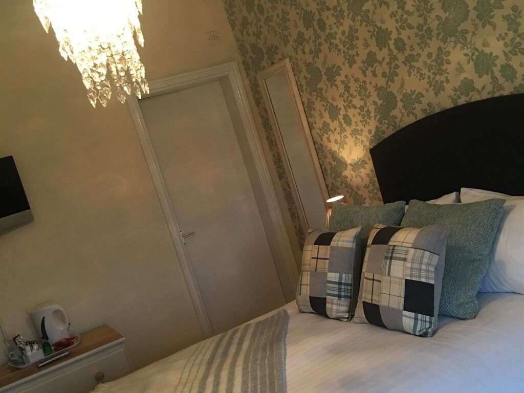 A bedroom with a bed, pillows, a bedside table, a nightstand, a wall-mounted TV, and a door.
