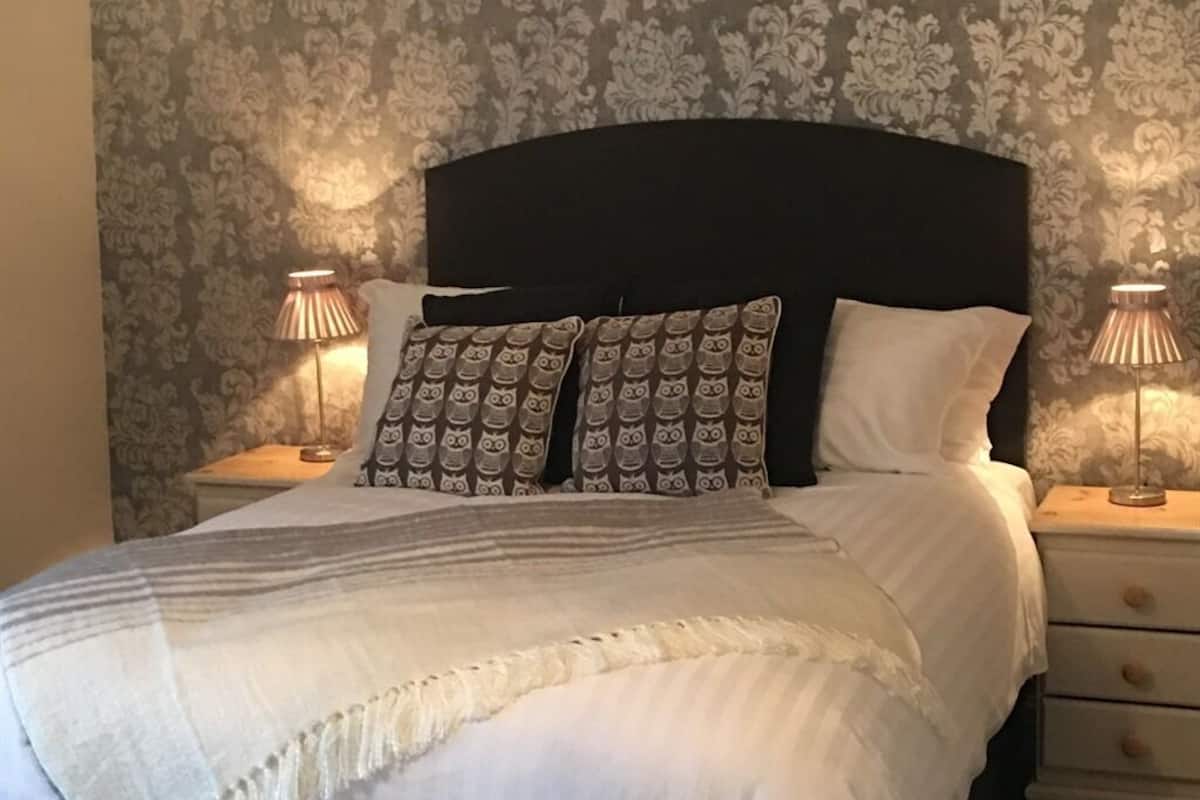A neatly made bed with a dark headboard, two bedside lamps, and patterned pillows.