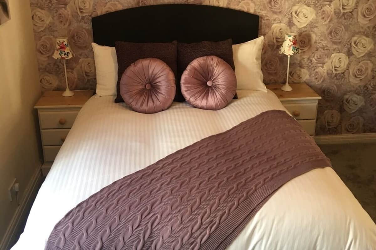 A neatly made bed with a patterned headboard, two bedside tables with lamps, and a floral wallpaper background.