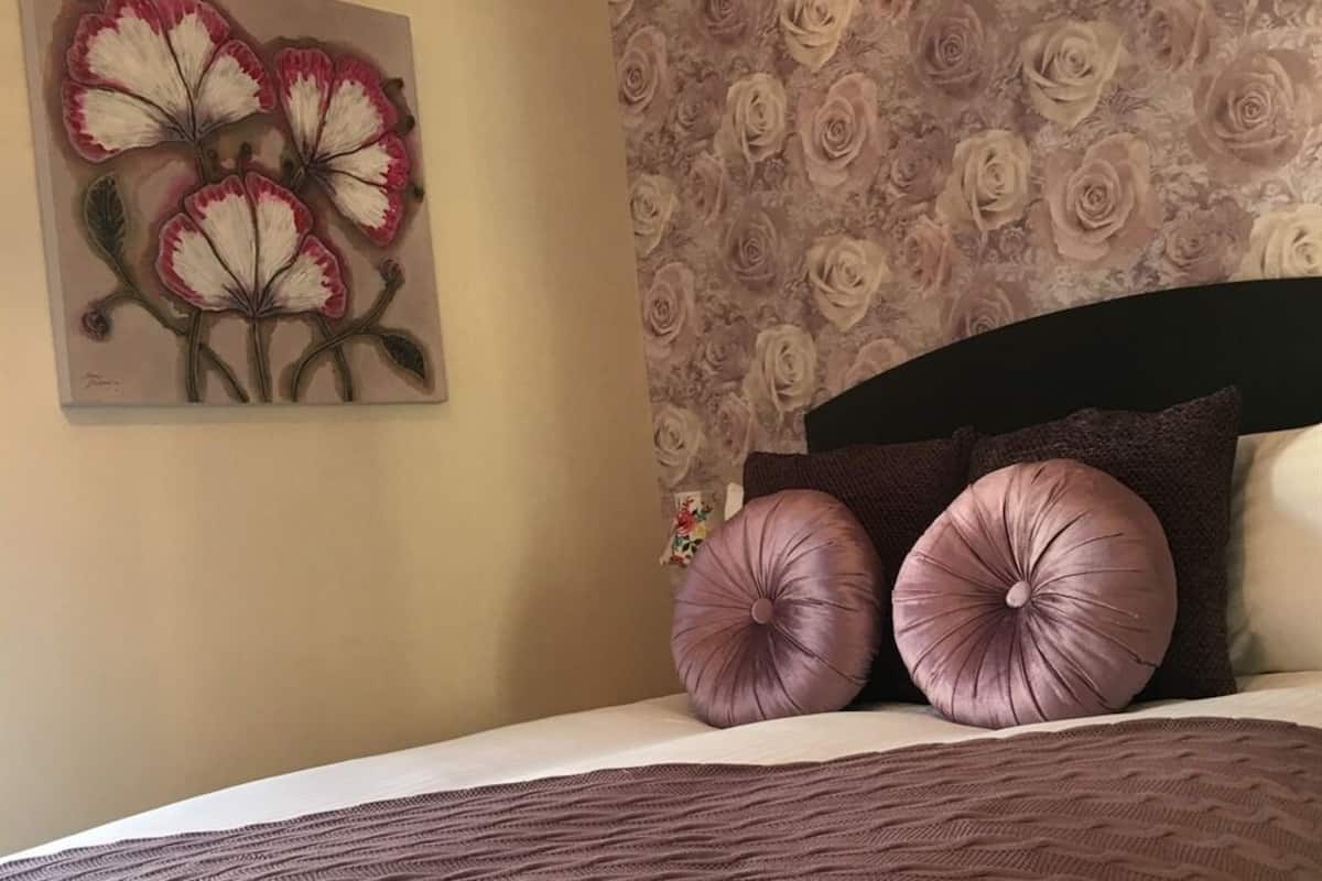 A bed with a brown headboard, two large purple pillows, and a floral painting on the wall.