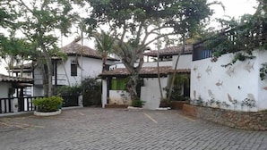 Un patio con pavimento de adoquines, un edificio blanco con techo de tejas y un árbol en el centro.