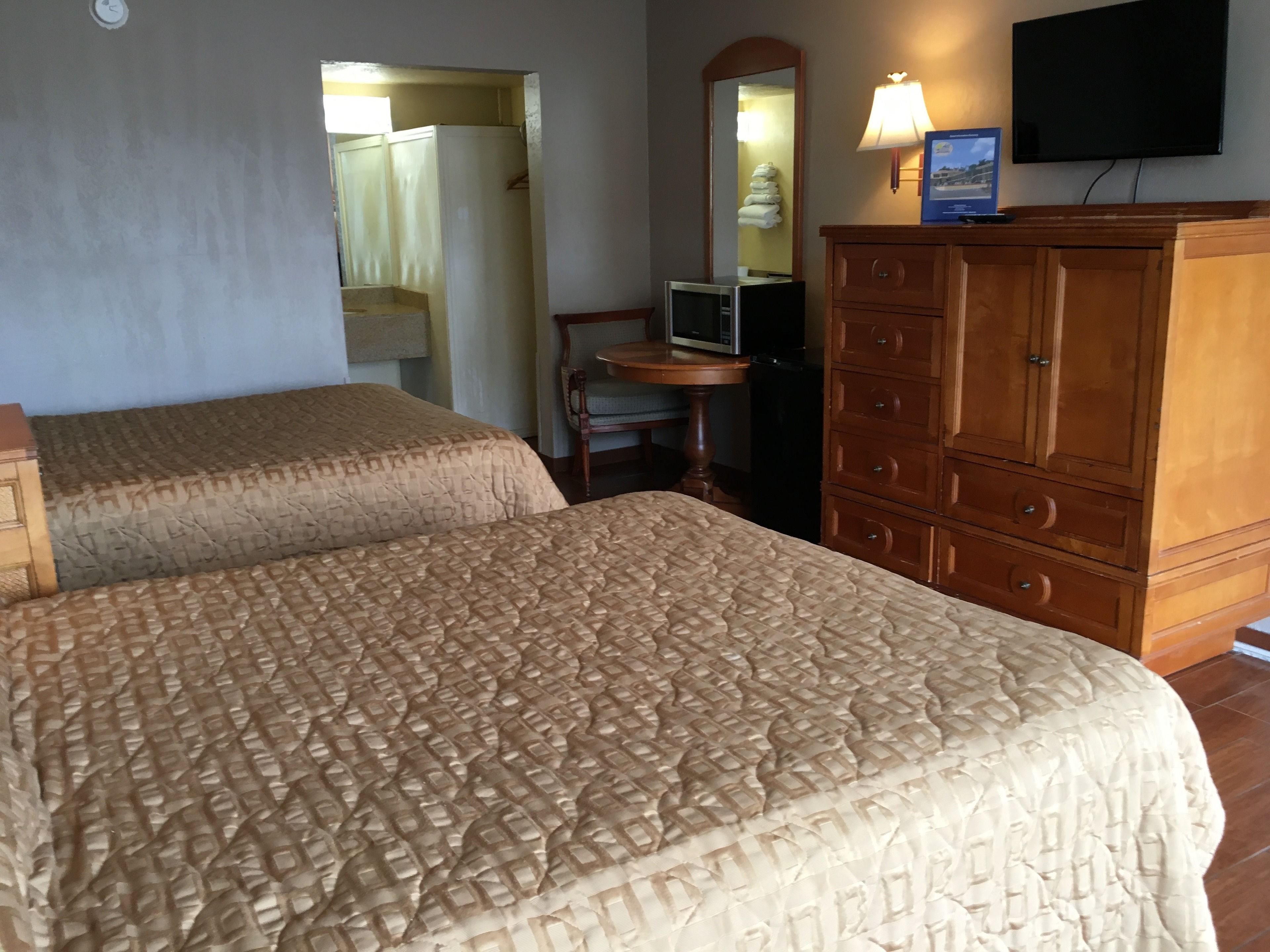 A hotel room with two beds, a wooden dresser, a television, and a mirror.