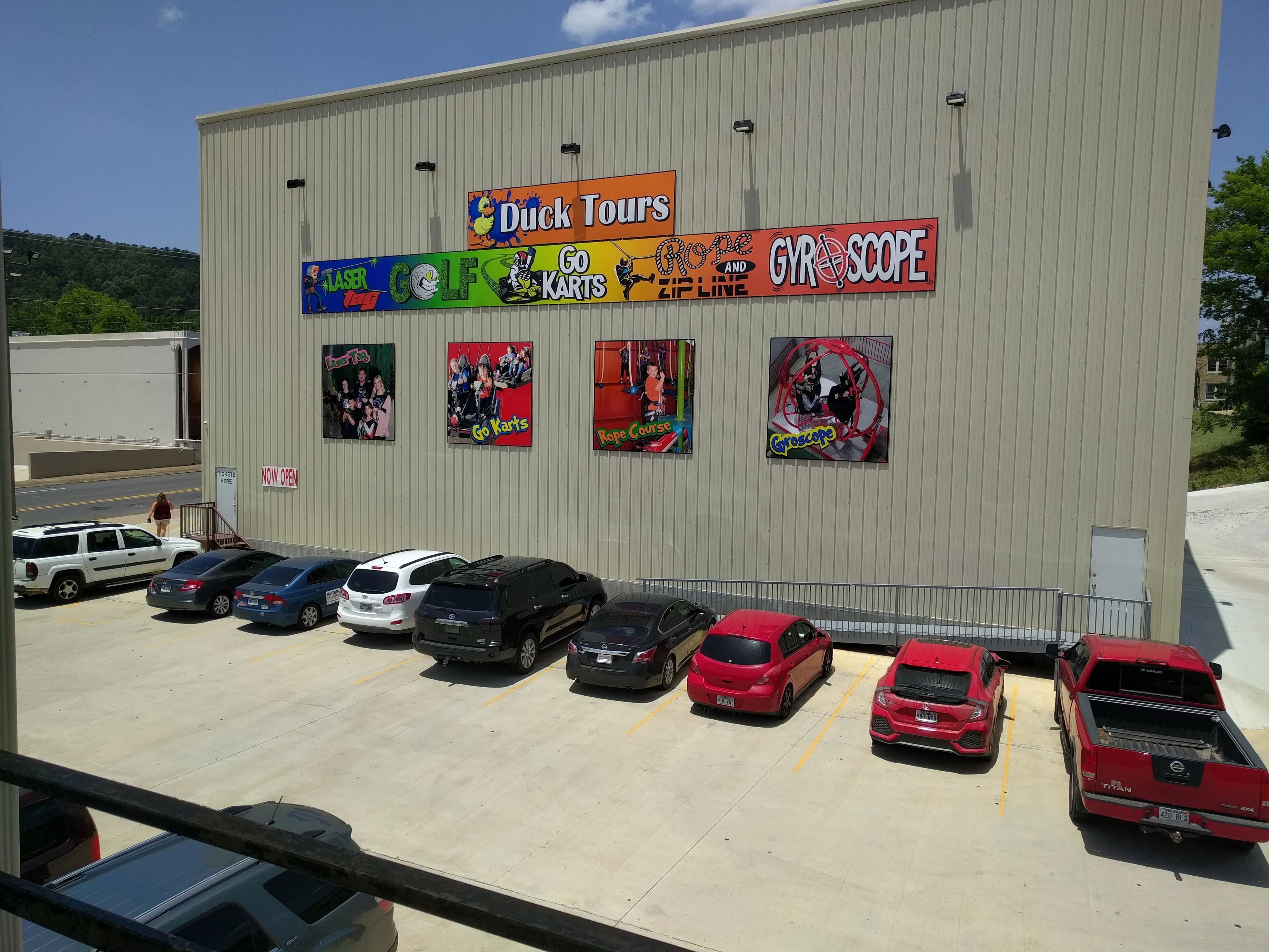 A building with multiple signs advertising activities like laser tag, golf, go-karts, rope courses, and a gyroscope. There are several cars parked in front.