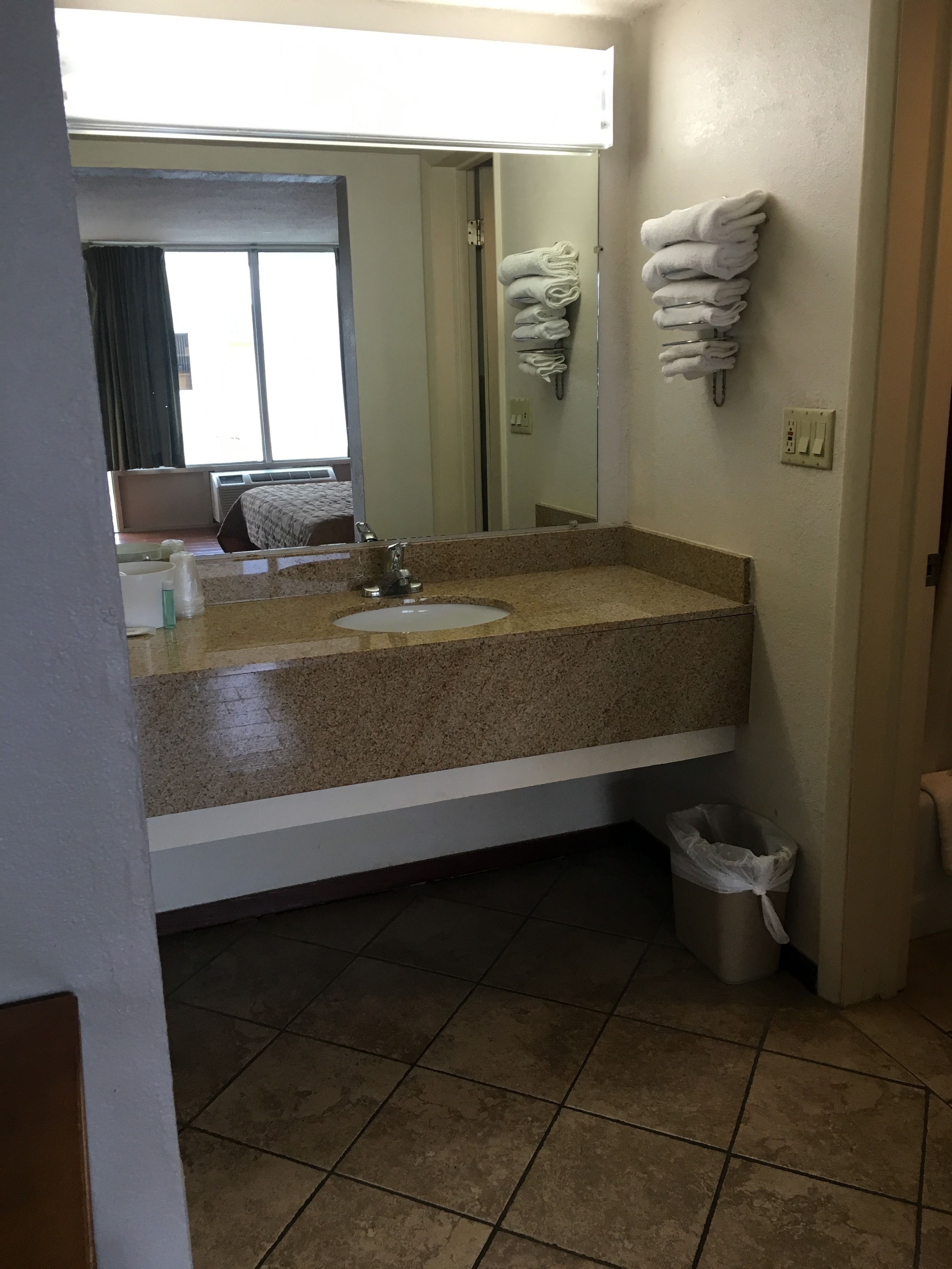 A bathroom with a granite countertop sink, a mirror, a towel rack, and a trash bin.