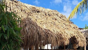 A thatched-roof structure with a wooden fence, gravel ground, and tropical vegetation. - BnBBonaire (Kralendijk)