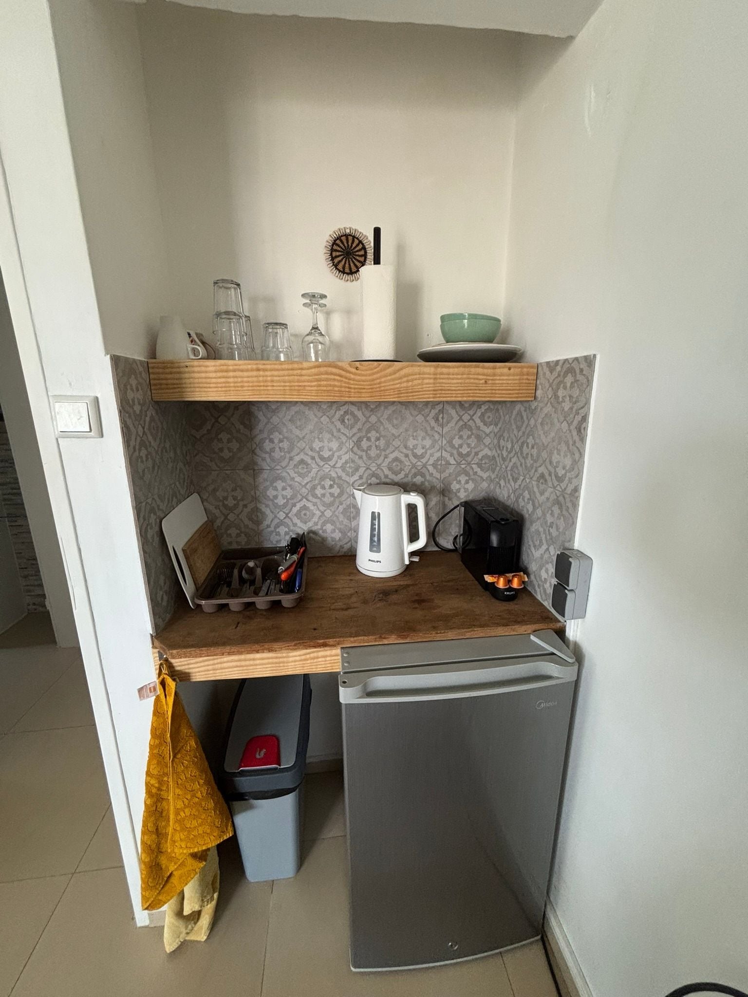 A compact kitchen with a refrigerator, a kettle, a coffee maker, and a sink.