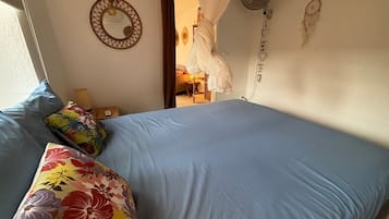 A bedroom with a bed, pillows, a bedside table, a wall-mounted mirror, a hanging light fixture, and a ceiling fan.