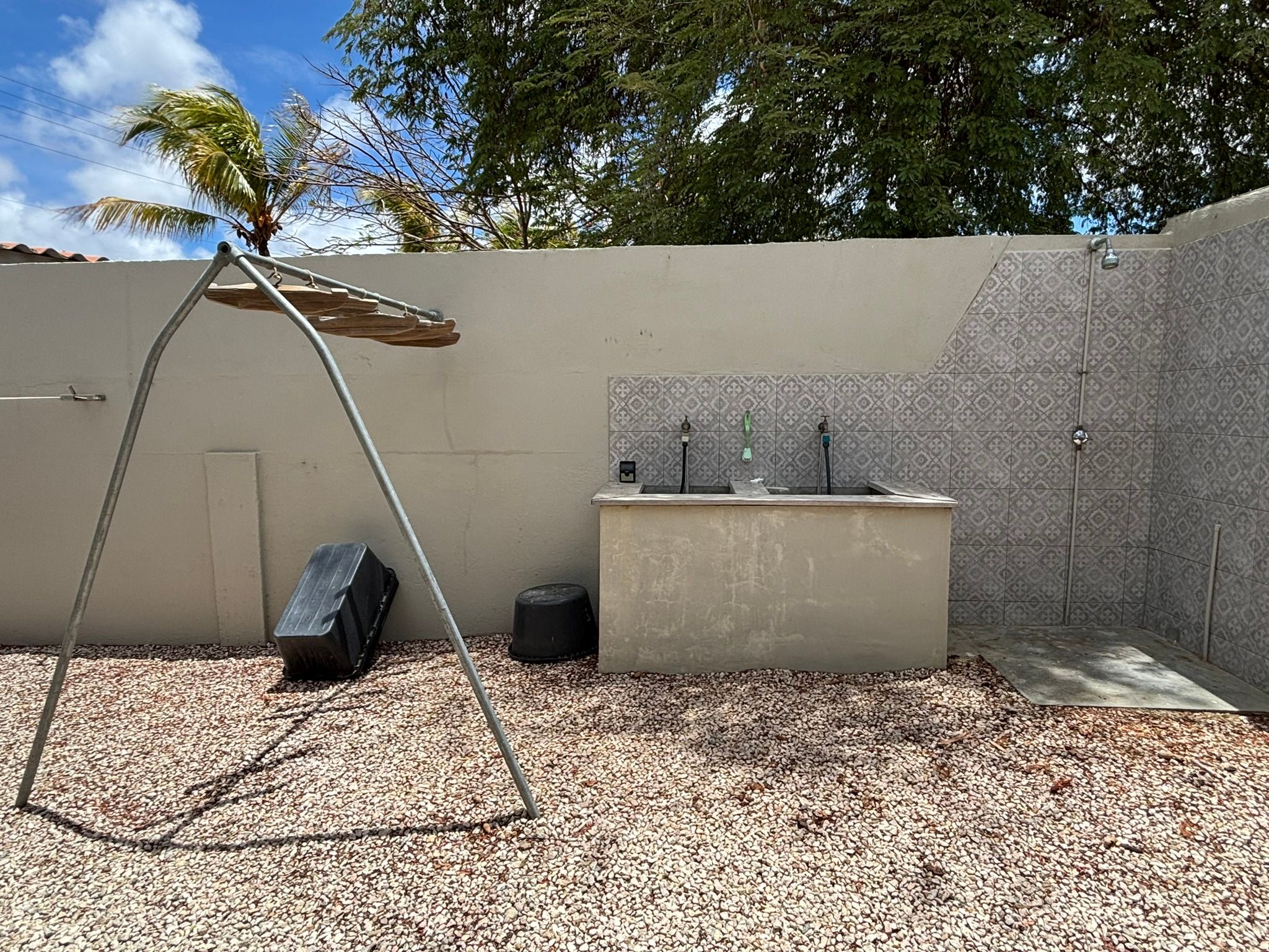 A small outdoor area with a concrete bench, a metal swing, and a tiled wall.
