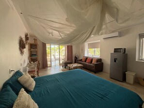 Een kamer met een bed, een bank, een tafeltje, een koelkast en een raam.
