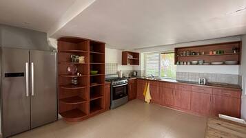 A kitchen with a built-in oven, a refrigerator, wooden shelves, and a window with blinds.