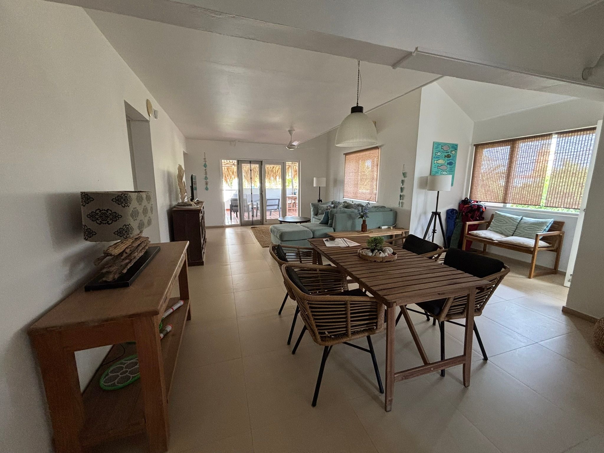 A spacious living area with a dining table, chairs, sofas, and a large window with blinds.
