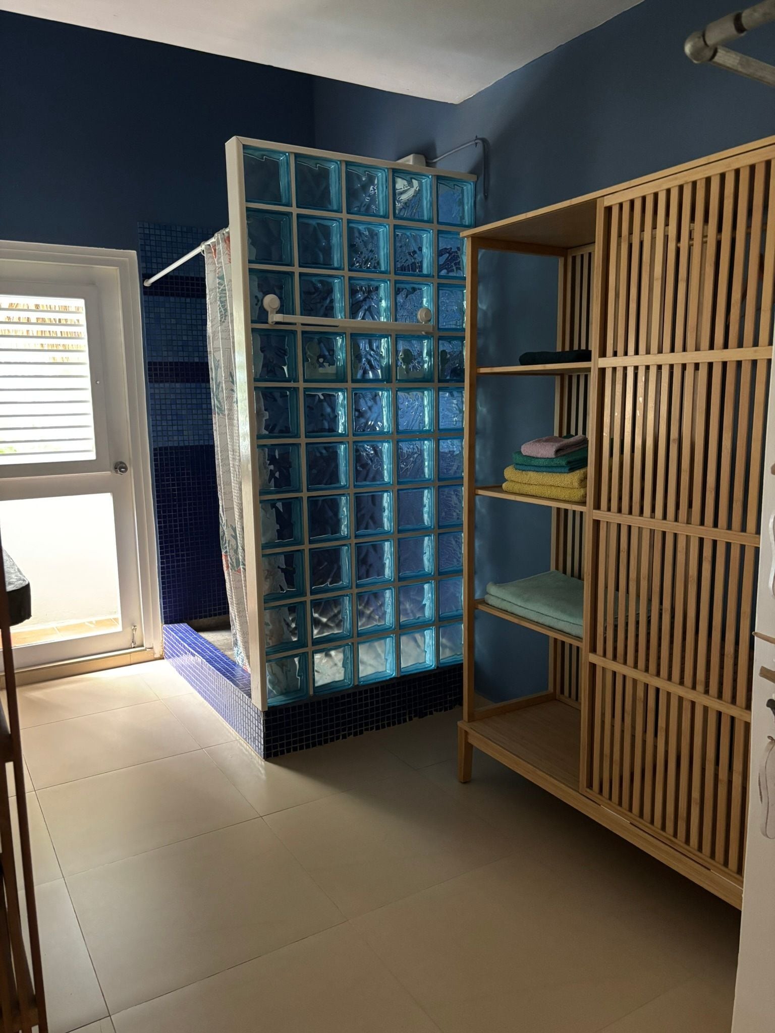 Una habitación con cabina de ducha de azulejos azules, un armario de madera y una puerta que da a un espacio exterior.