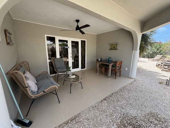 A covered patio area with a ceiling fan, wicker furniture, a small table, and a dining set.