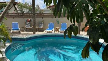 A swimming pool with blue tiles, surrounded by lounge chairs and tropical plants.