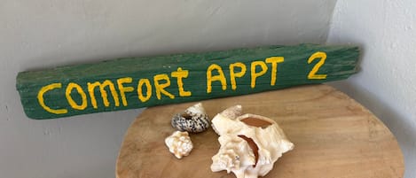 Un banc en bois avec une plaque verte au-dessus, sur laquelle on peut lire : « APPARTEMENT CONFORT 2 ».