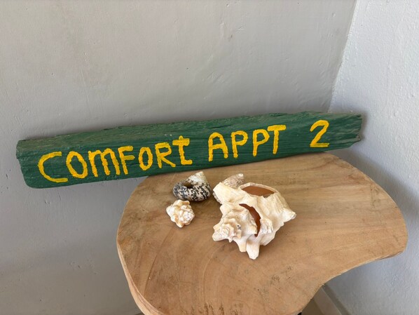 Un banc en bois avec une plaque verte au-dessus, sur laquelle on peut lire : « APPARTEMENT CONFORT 2 ».