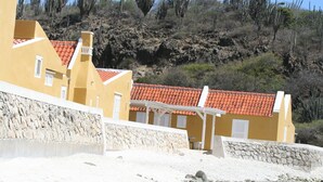 A coastal building with a red-tiled roof, white balconies, and a stone wall. - BnBBonaire (Kralendijk)