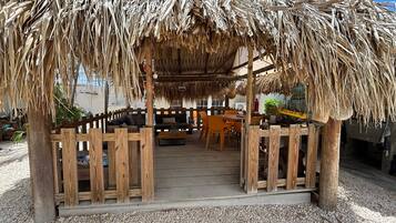 A thatched-roof outdoor seating area with wooden furniture and a gravel floor.
