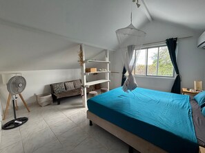 Une chambre à coucher avec un lit, un ventilateur sur pied, un canapé et une fenêtre avec des rideaux.