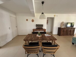 Een eetgedeelte met een houten tafel en rieten stoelen, een hanglamp en een televisie op een houten kast.