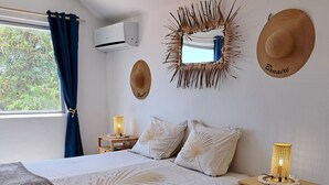 A bedroom with a bed, bedside tables, a wall-mounted mirror, and decorative hats. - BnBBonaire (Kralendijk)