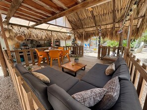 An outdoor seating area with a thatched roof, wooden furniture, and a view of the surrounding landscape.