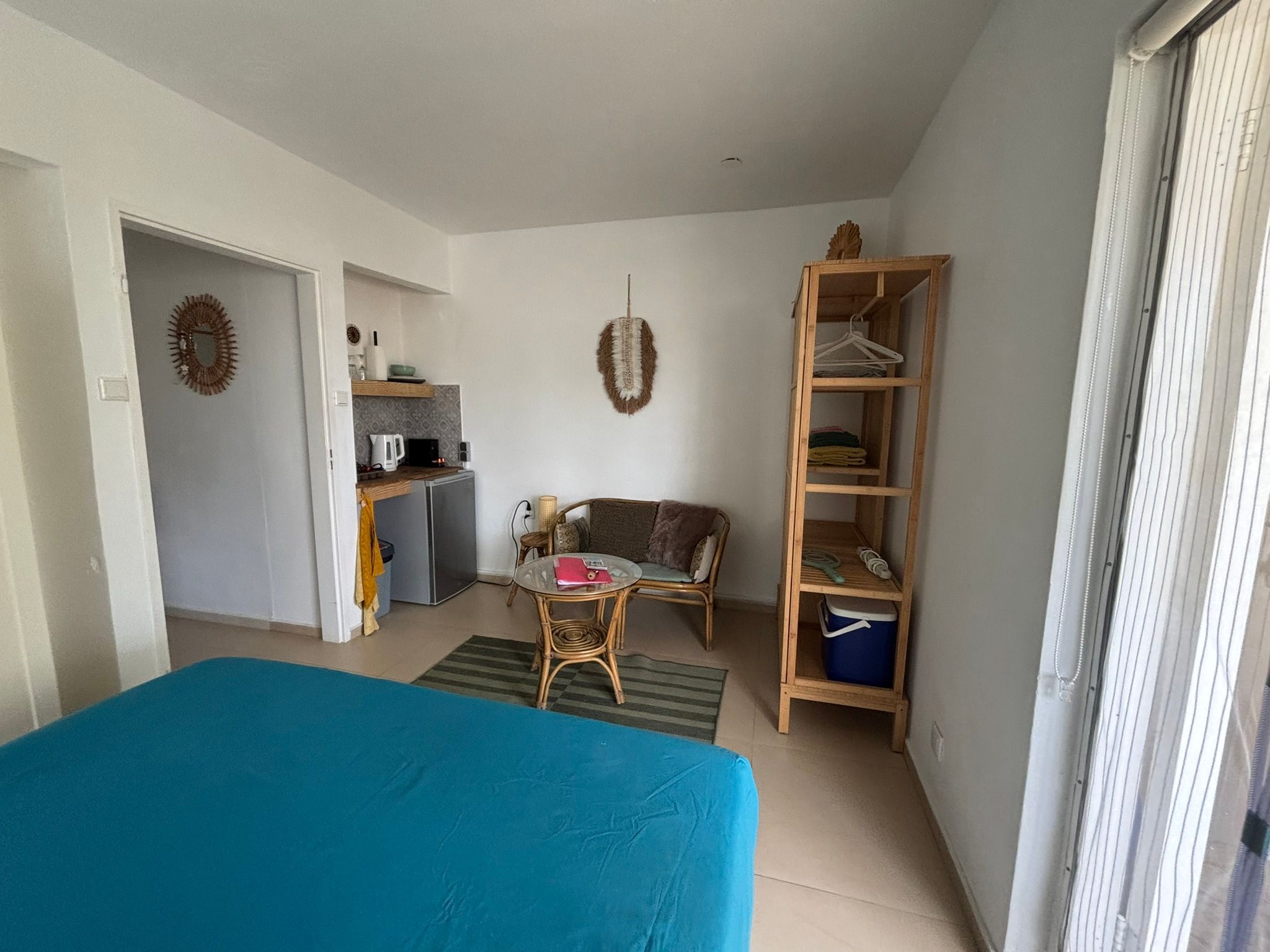 A compact room with a bed, a small table, a sofa, a kitchenette, and a wardrobe.