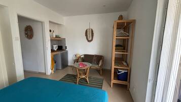 A compact room with a bed, a small table, a sofa, a kitchenette, and a wardrobe.