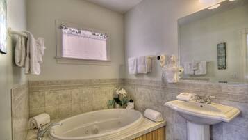 A bathroom with a bathtub, a sink, and a large mirror. There are towels hanging on the wall and a window with a curtain.