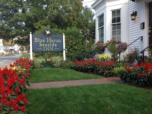 A Blue Heron Seaside Inn sign with a bird logo, surrounded by vibrant flower beds and a brick pathway. - Blue Heron Seaside Inn (Boothbay Harbor)