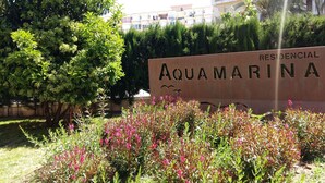 Señal de 'AQUAMARINA' con un jardín exuberante al frente.