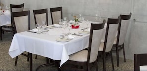 A dining table set for six with white tablecloths, dark chairs, and glassware.