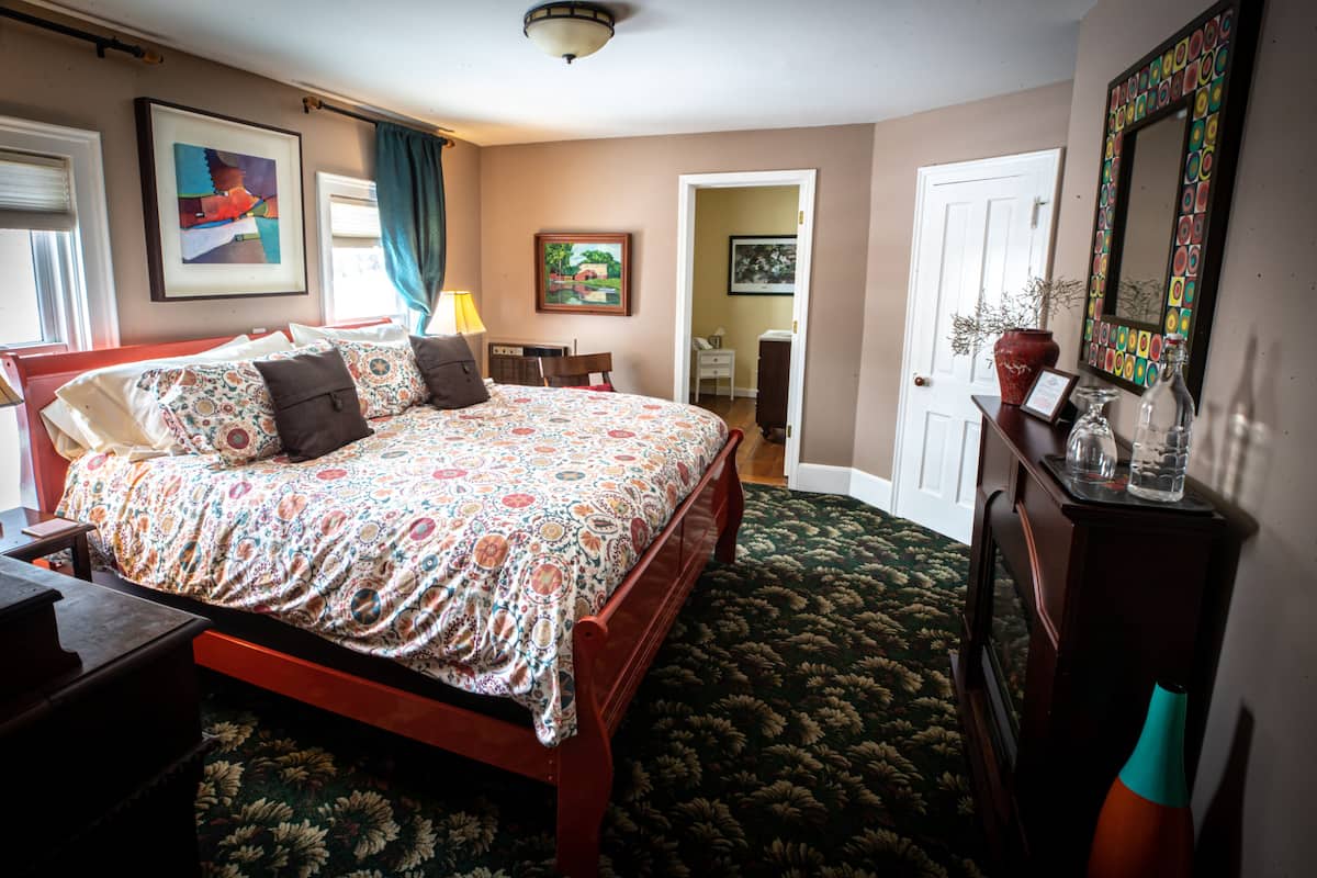 A bedroom with a bed, dresser, and a door leading to another room.