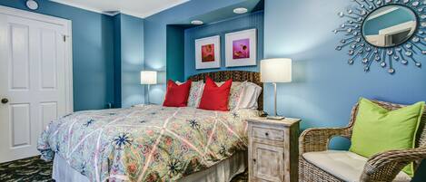 A bedroom with a bed, nightstand, chair, and wall art.