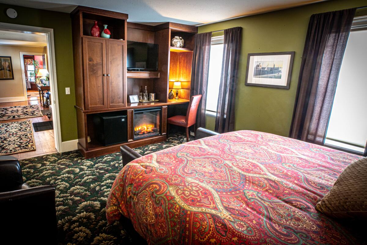 A hotel room with a large bed, a fireplace, a television, and a view of the city through the window.