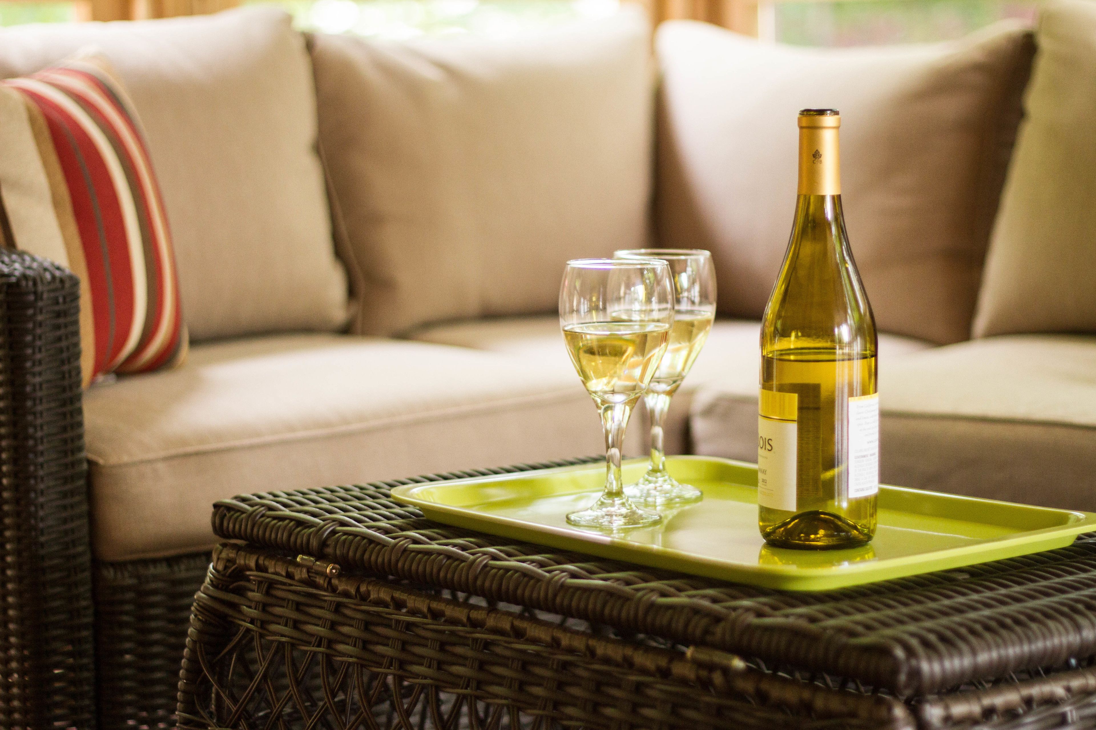 A wicker table with a green tray holding a wine bottle and two glasses.