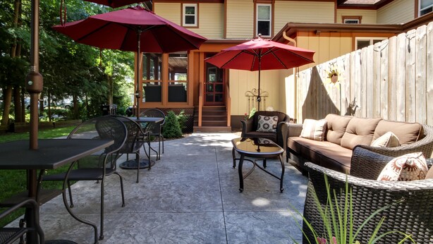 A patio area with outdoor furniture, including a table and chairs, and two red umbrellas providing shade. - Twin Oaks Inn (Saugatuck)
