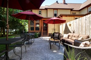 A patio area with outdoor furniture, including a table and chairs, and two red umbrellas providing shade. - Twin Oaks Inn (Saugatuck)