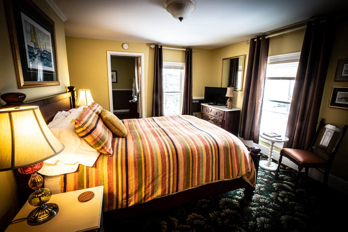 A hotel room with a large bed, a desk, a chair, a television, and a window with curtains.