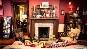 A cozy living room with a fireplace, leather sofa, armchairs, and a bookshelf. - Twin Oaks Inn (Saugatuck)