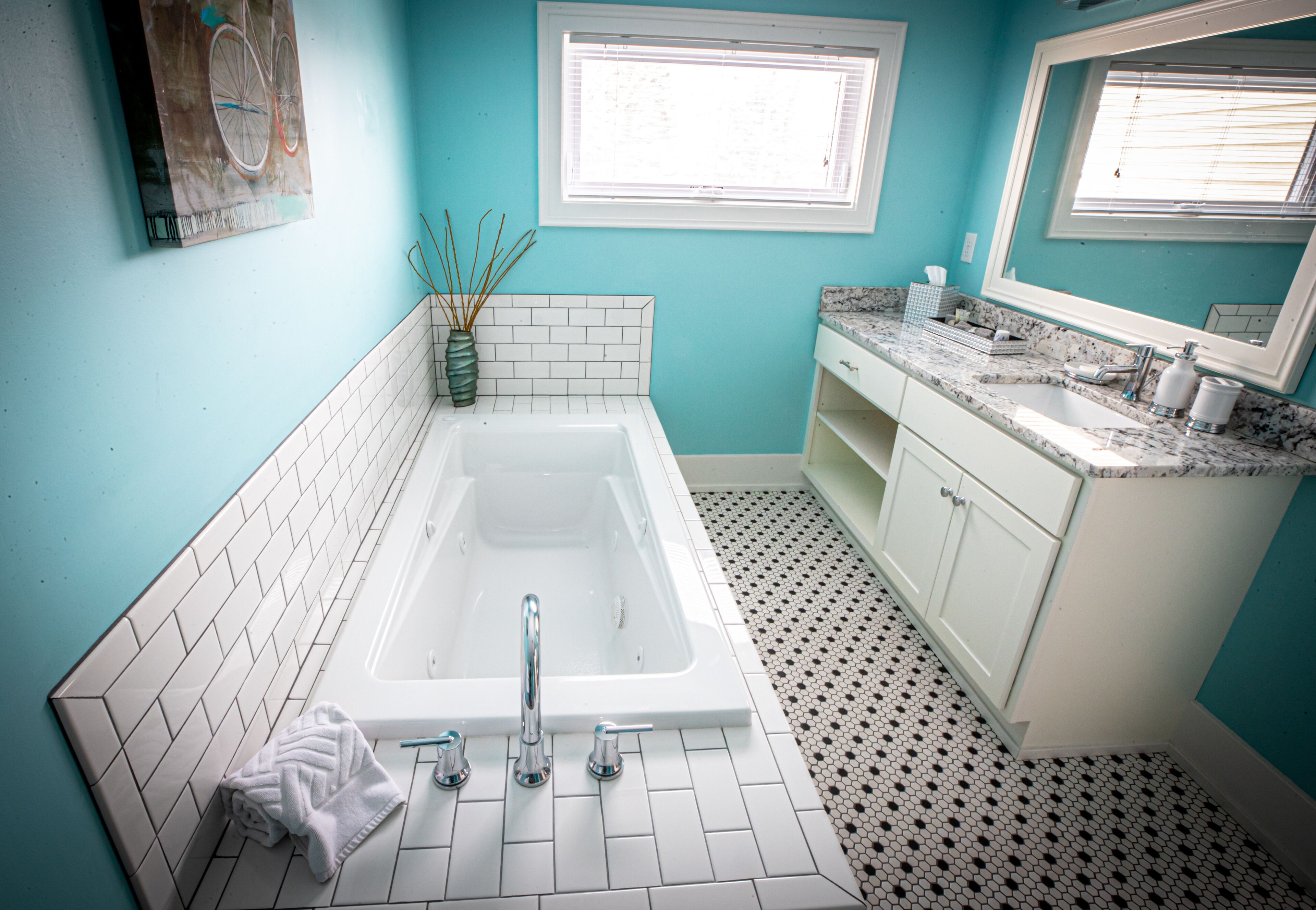 A bathroom with a white bathtub, a sink with a marble countertop, and a window with blinds.