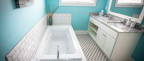 A bathroom with a white bathtub, a sink with a marble countertop, and a window with blinds.