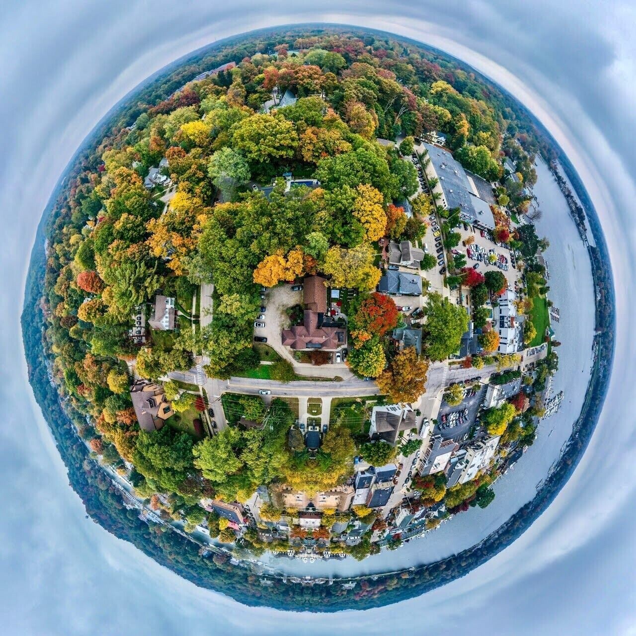 Une vue aérienne circulaire d’un quartier résidentiel, avec des maisons, des routes et une étendue d’eau.