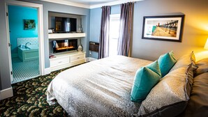 A bedroom with a large bed, a fireplace, a television, and a bathroom with a blue wall and white tiles. - Twin Oaks Inn (Saugatuck)