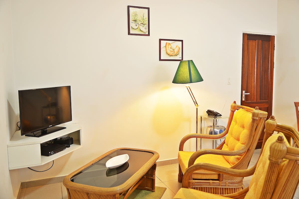 A living room with a television, a green lamp, wicker chairs, and a wooden door.